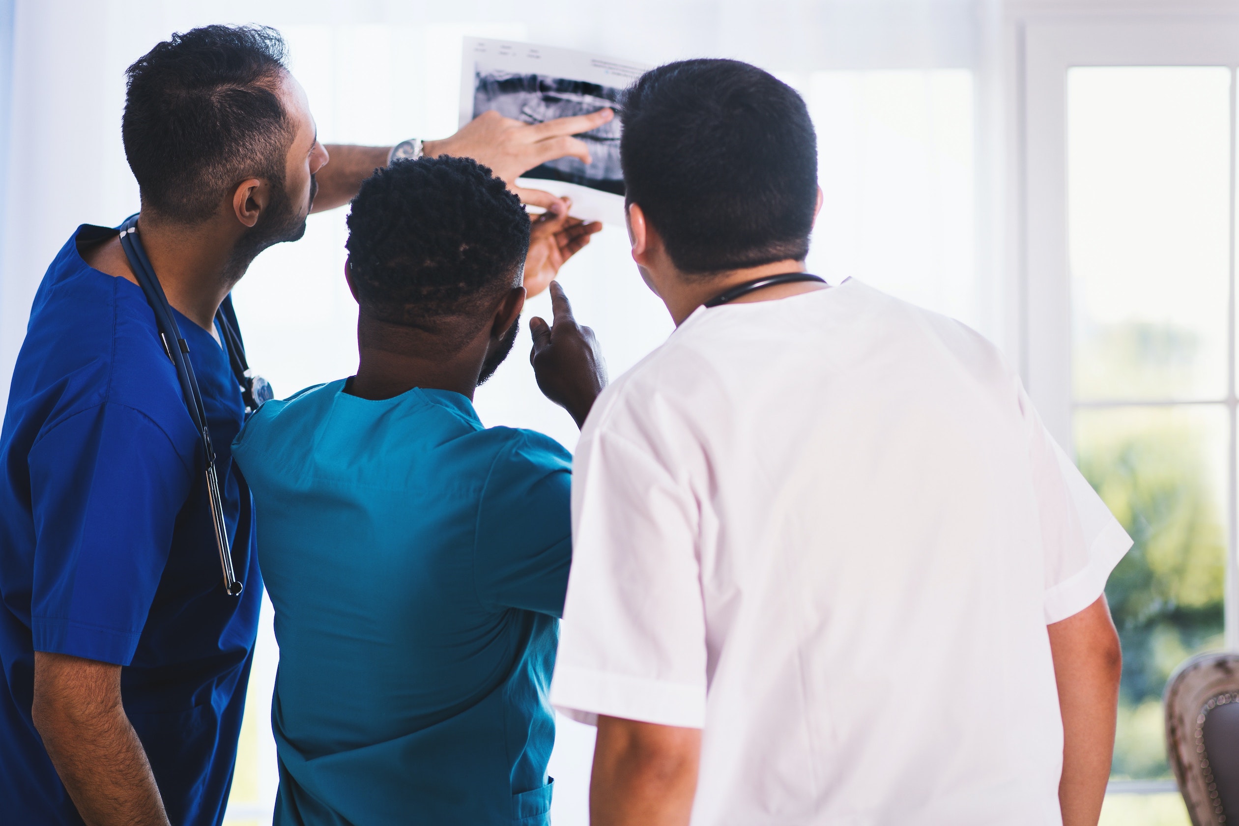 Three male doctors reviewing medical chart during clinical study conduct wearing scrubs in clinical setting