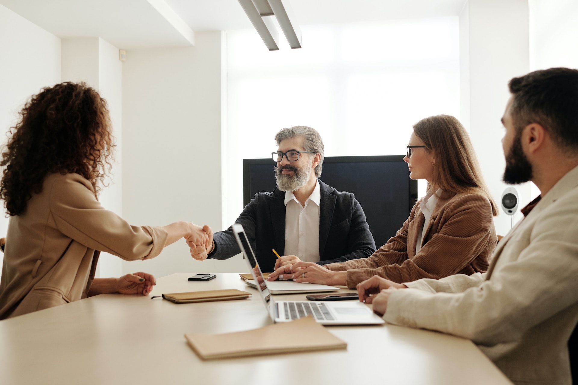 CRO professional woman with dark curly hair shaking hands with job interviewer panel at a wood table